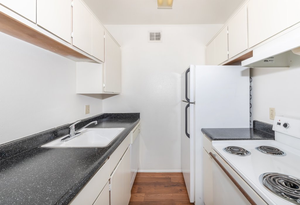Apartment kitchen with white cabinetry, a refrigerator and a range.